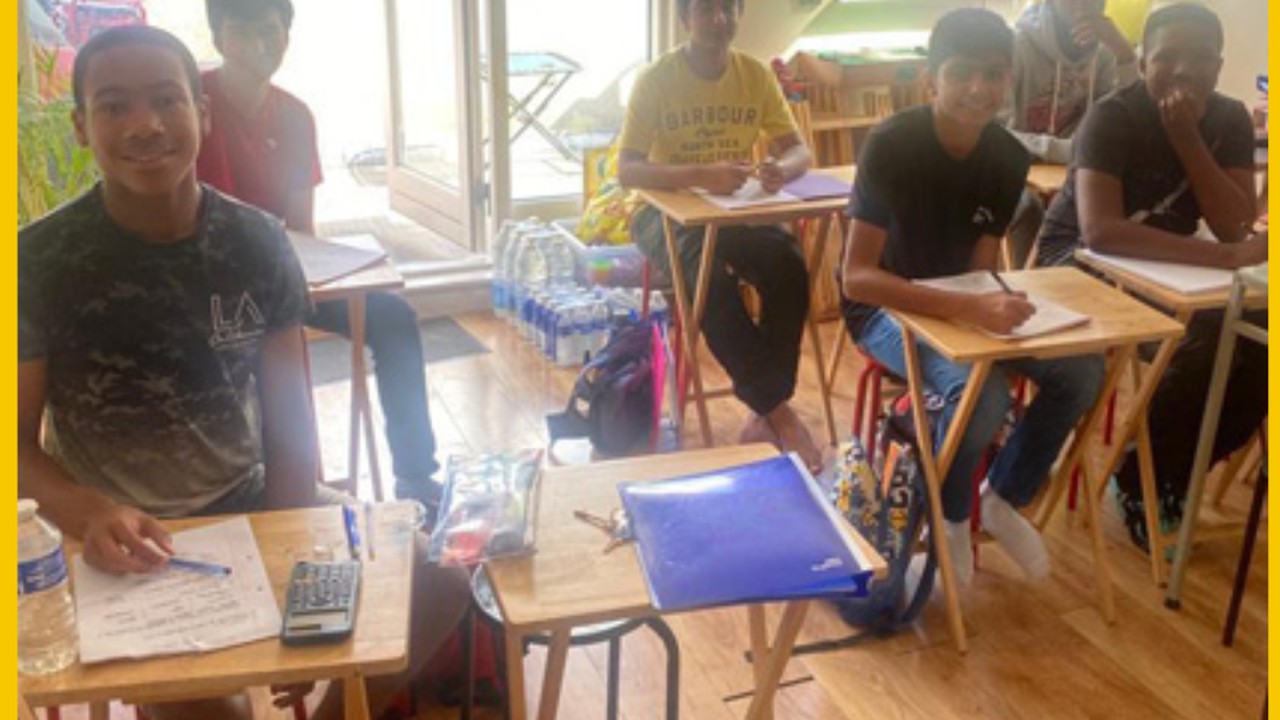 The studio mid-session a young builder at a laptop, mentor leaning in, others working nearby